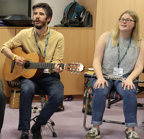 Caucasian man with short dark hair and beard playing guitar next to a blonde caucasian woman
