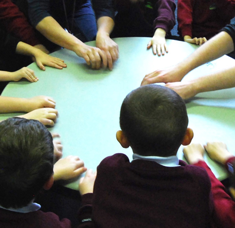 several adult and child hands gather round a large drum